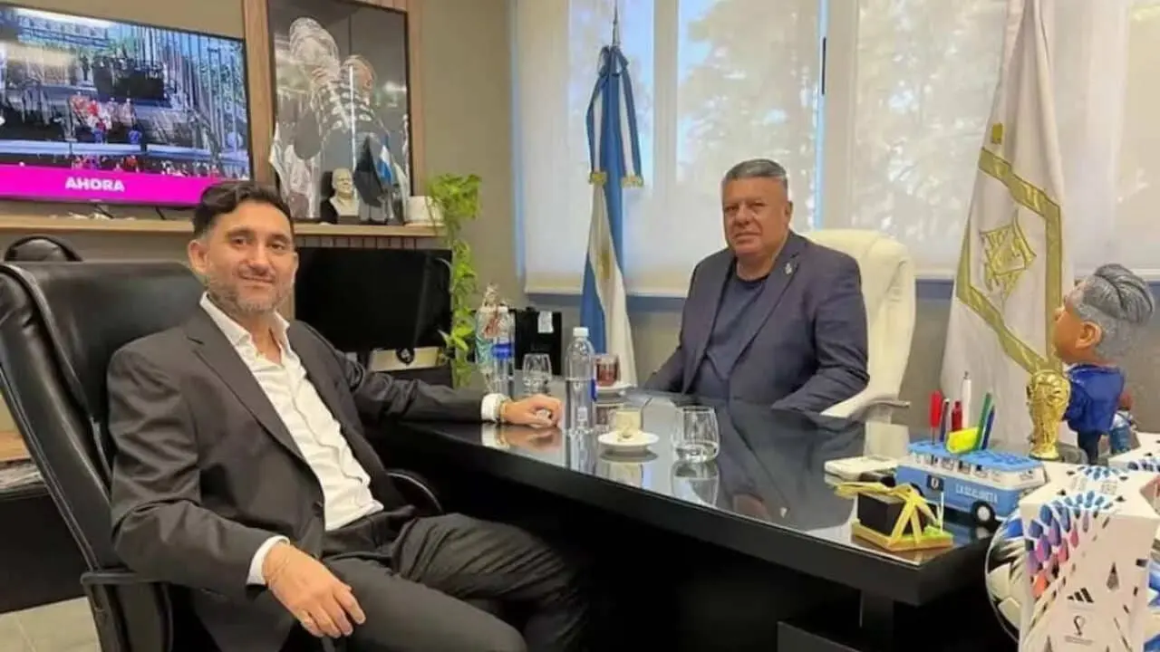 Ariel Vallejo sentado frente al escritorio de Chiqui Tapia, quien está también